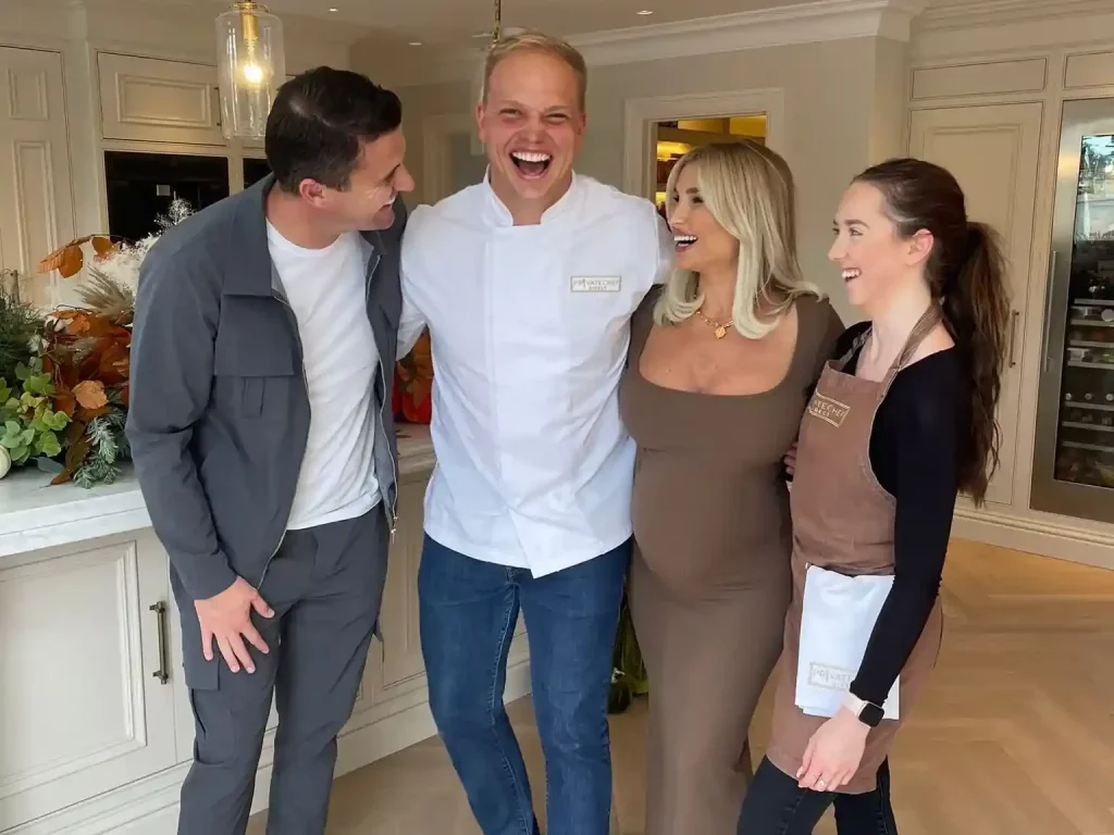 A chef stands with 3 diners, they are laughing